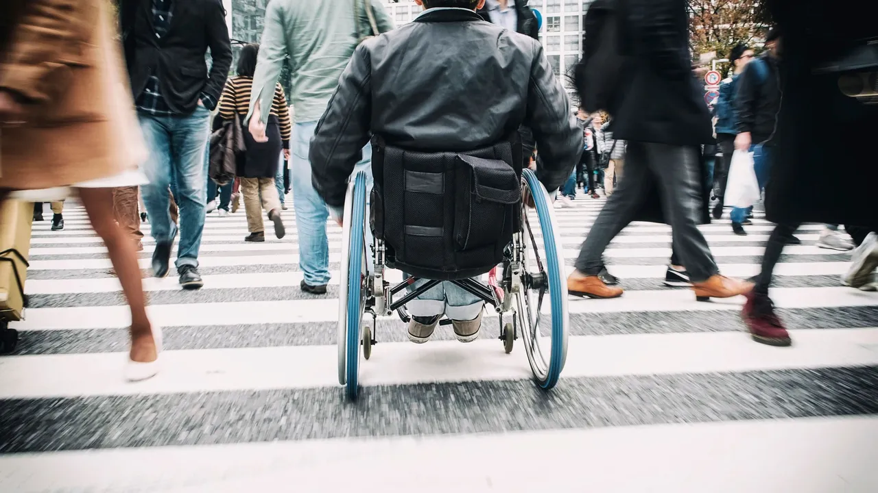 View from behind a man in a wheelchair in a busy crosswalk. 