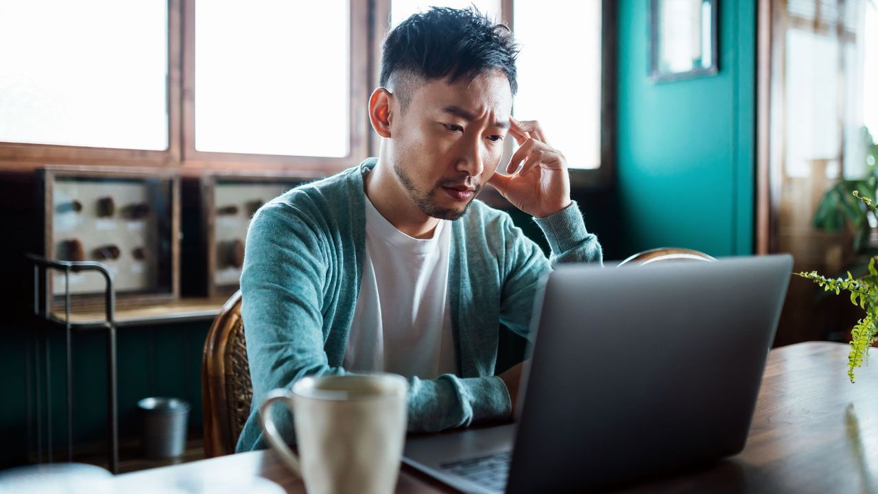 A frustrated young graduate applying for jobs on a laptop in a coffee shop, symbolizing the modern job search struggle. (co.uk)