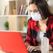 Stock image of a masked woman typing on a laptop thumbnail