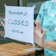 File image of woman placing a 'Closed' sign on a cafe thumbnail