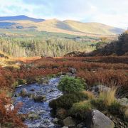 A stream trickles between two hills with mountains in the background thumbnail