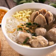 A spoon, sauce, and a bowl of mie bakso on a table thumbnail