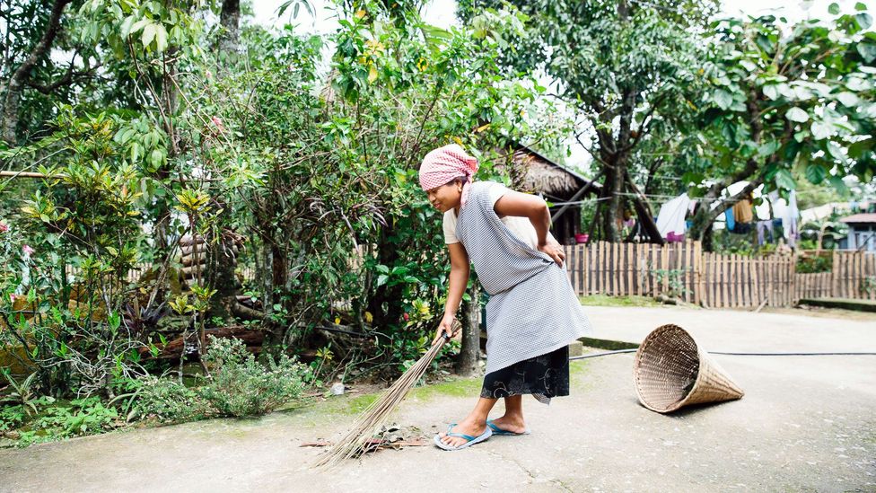 A woman sweeps debris into a cone-shaped wastebasket in Mawlynnong (Credit: Tanveer Badal)