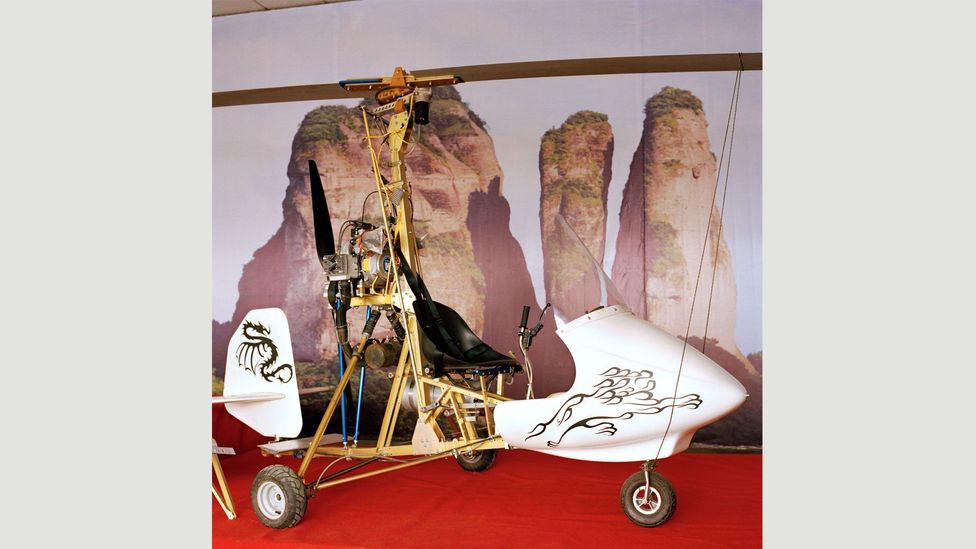 Xu’s autogyro next to a poster of nearby Jianglang Mountain: “I love flying [there]… I make it to the edge of the mountain and then hover along its ridges.” (Credit: Xiaoxiao Xu)