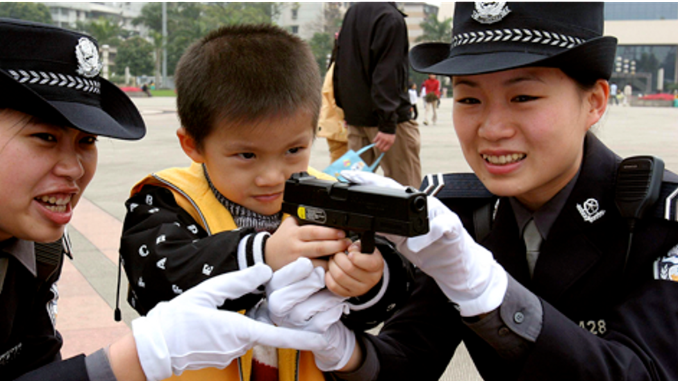 Members of the Policewoman Bicycle Patrol Team show a gun to a young boy in Nanning, China. (Credit: Getty Images)