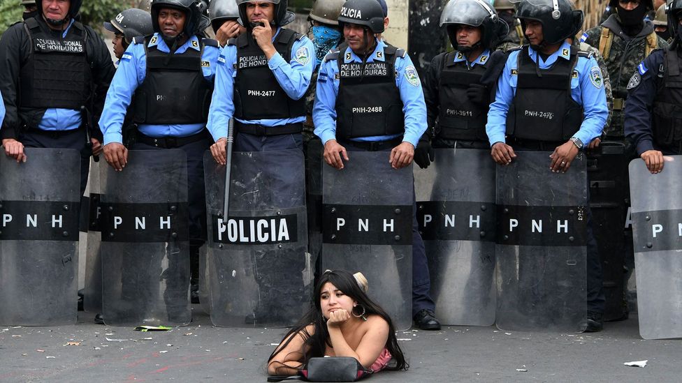 A protestor lies on the street in front of police officers during a demonstration against the contested re-election of President Hernandez in Honduras (Credit: Getty Images)