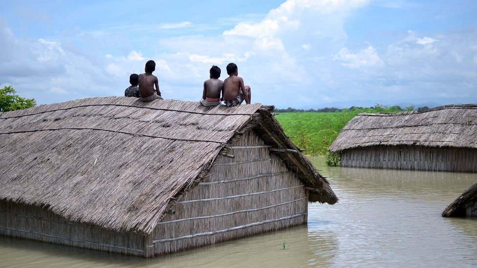 Children sit on the roof of a submerged home after a 2016 flood of the Brahmaputra River in South Kamrup, India (Credit: Getty Images)