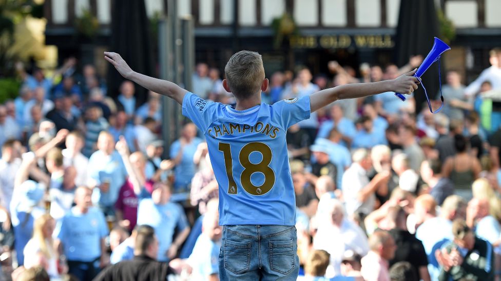 A young Manchester City fan waits with thousands of other fans to watch his team parade the Premier League trophy (Credit: Getty Images)