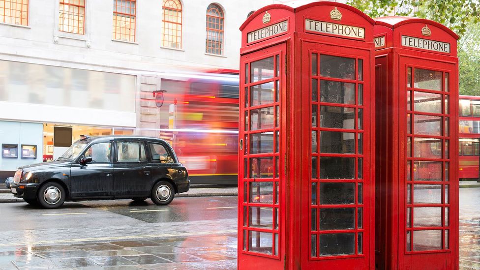 Two red telephone booths on a London street with a double-decker bus and a black taxi