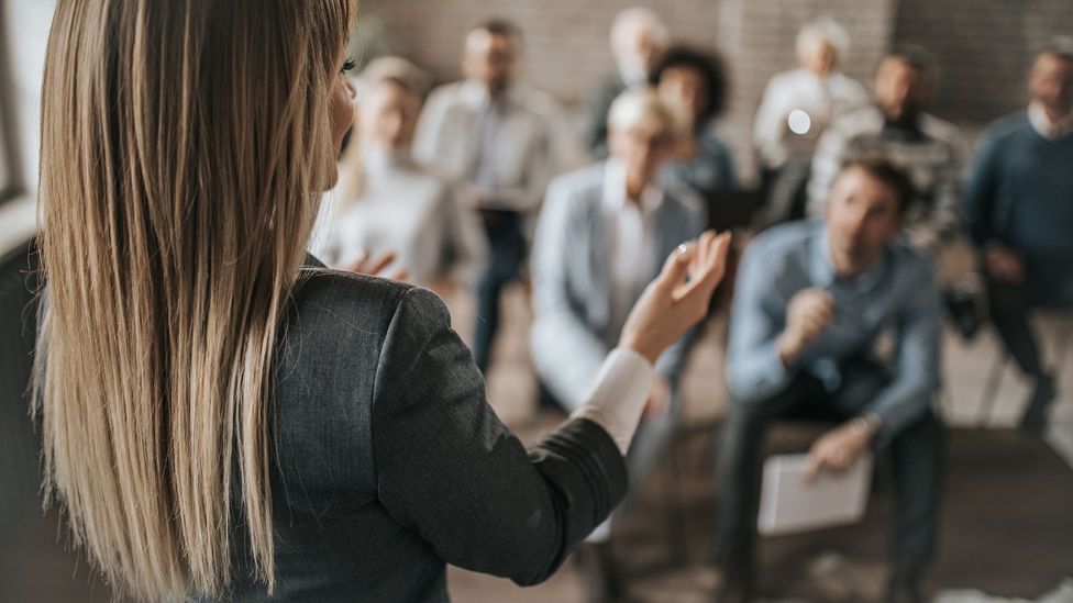 Woman speaking to crowded room (Credit: Getty Images)