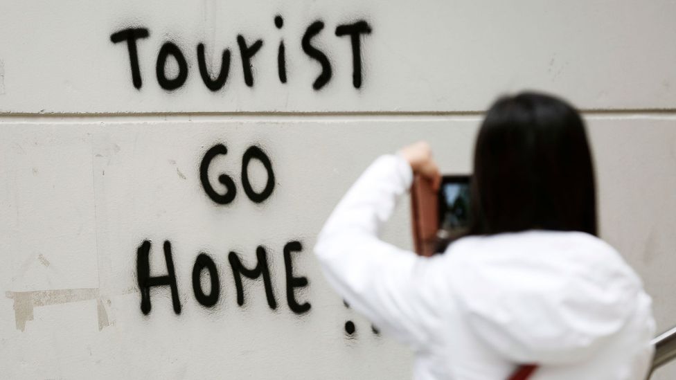 A tourist taking a photo of graffiti telling tourists to go home in Barcelona, Spain last year (Credit: Getty Images)