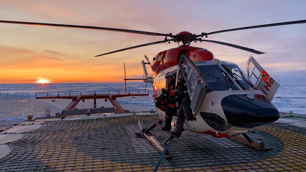 Expedition members sit in a BK-117 helicopter on board Polarstern, while a long-range Russian Mil Mi-8 flies in the background (Credit: AWI/Markus Rex) Expedition members sit in a BK-117 helicopter on board Polarstern, while a long-range Russian Mil Mi-8 flies in the background (Credit: AWI/Markus Rex)