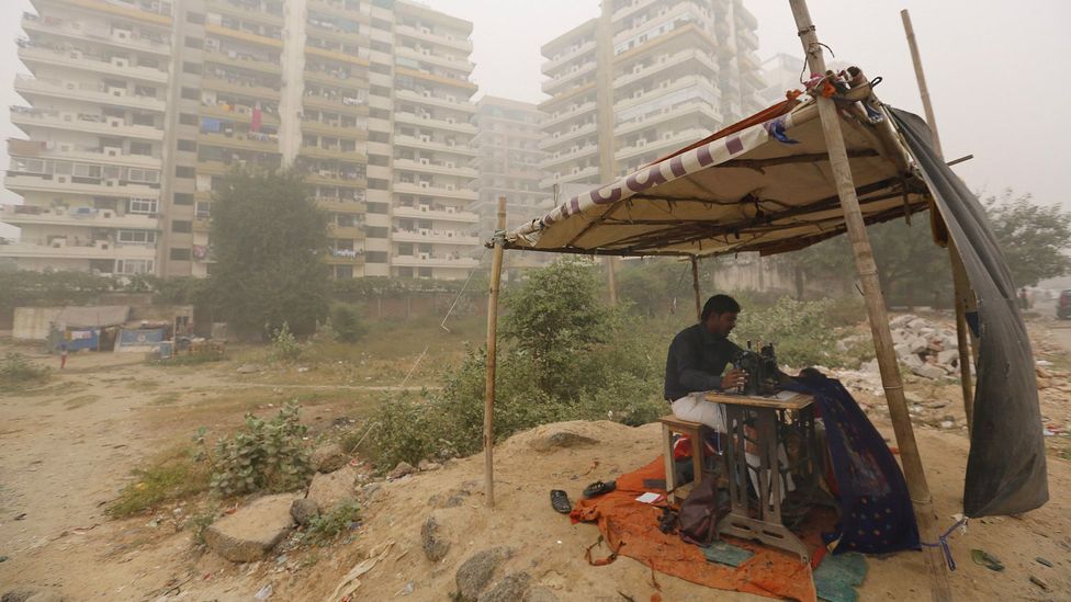 A roadside tailor stitches cloths in heavy smog in New Delhi, India; air pollution is linked to weakened respiratory health (Credit: Getty Images)