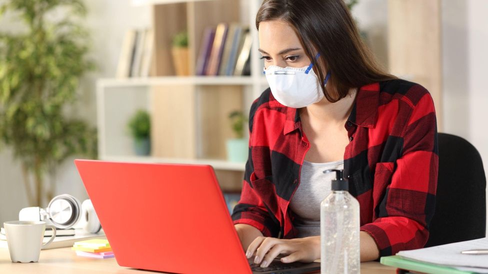 Stock image of a masked woman typing on a laptop