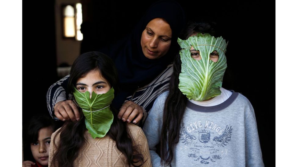 A Palestinian mother entertains her children with makeshift masks made of cabbage as she cooks in Beit Lahia in April 2020 (Credit: Mohammed Abed/AFP via Getty Images)