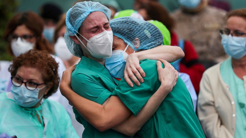 Health workers embrace following the death of a colleague in Spain (Credit: Susana Vera/Reuters)