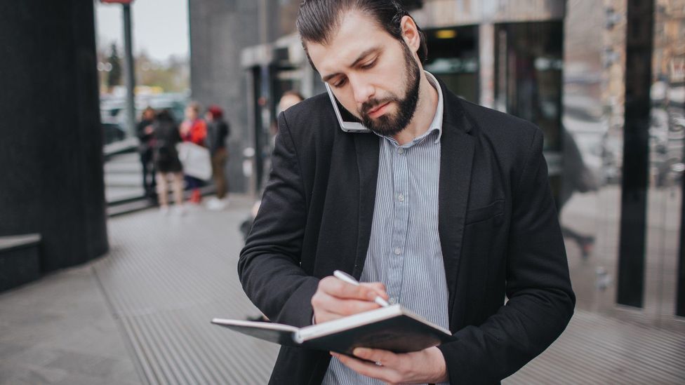 Man on phone writing notes while walking