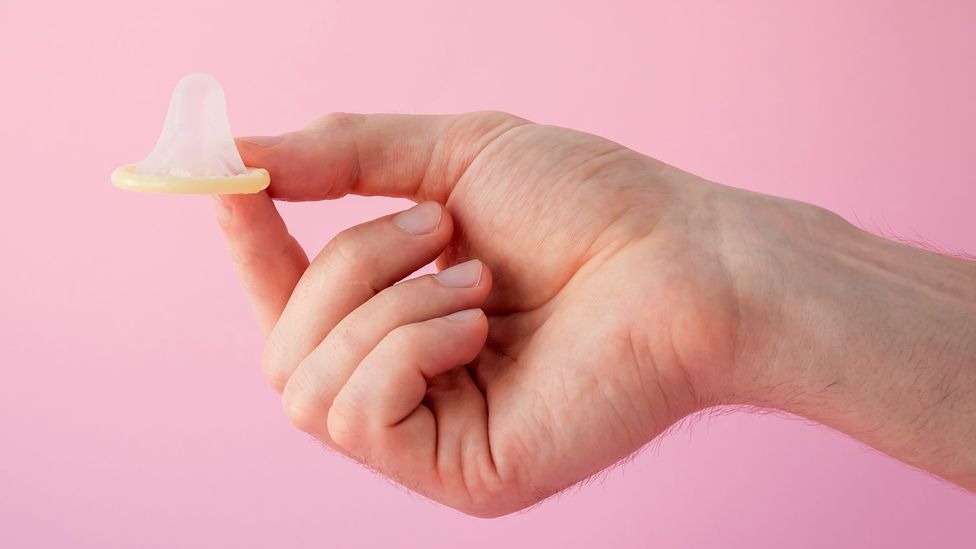 A condom held in front of a pink background (Credit: Getty Images)