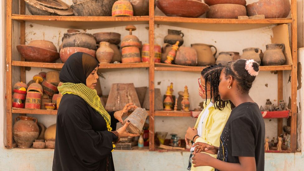 Amberkab uses a traditional copper weight to explain the traditional barter economy to Tarek and Merghany (Credit: Mai Farouk)