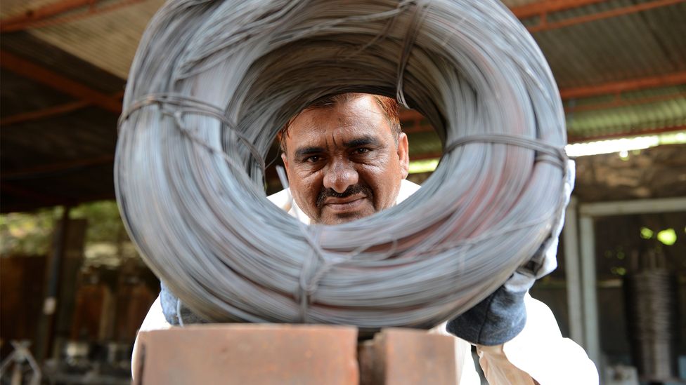 Niyazahmed Shaikh peers through coiled wires made from scrap steel strips in his factory in India (Credit: Sam Panthaky/Getty Images) Niyazahmed Shaikh peers through coiled wires made from scrap steel strips in his factory in India (Credit: Sam Panthaky/Getty Images)