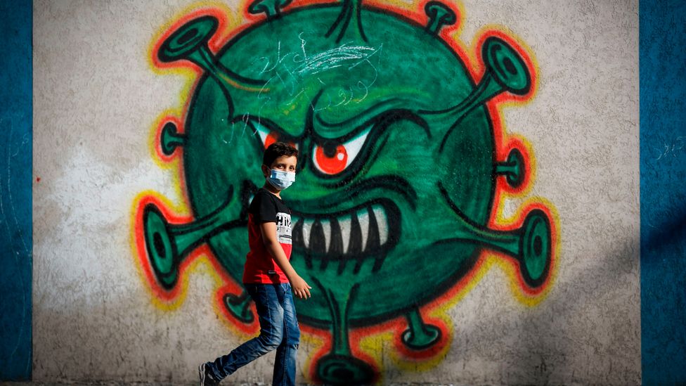 A boy walks past street art of Covid-19 virus (Credit: Mohammed Abed/Getty Images)
