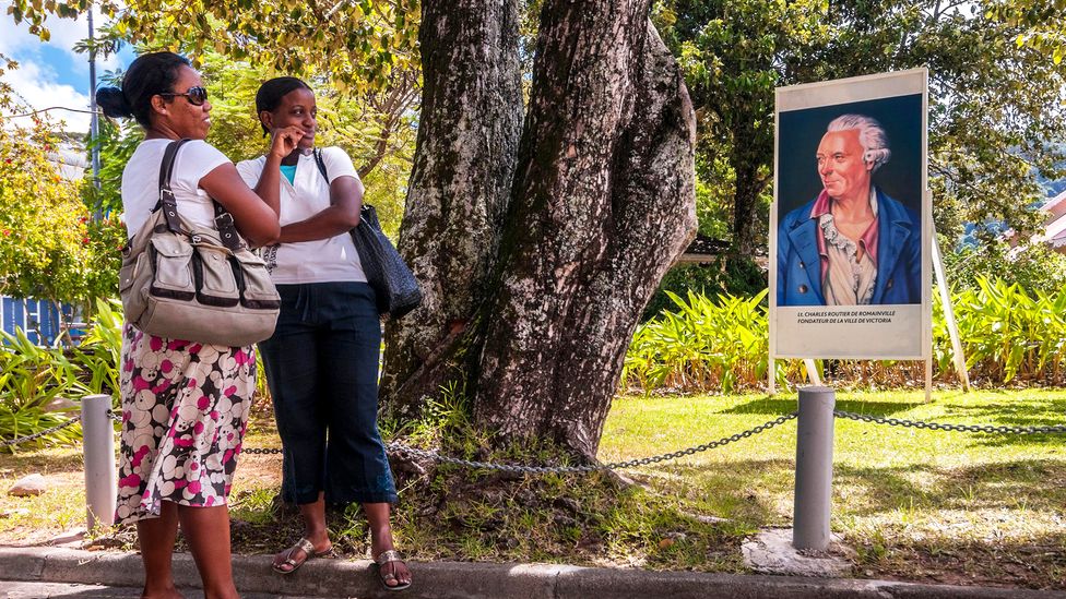 Women stop for a chat in front of an image of Lieutenant Charles Routier de Romainville, founder of the city of Victoria (Credit: Hemis/Alamy Stock Photo)
