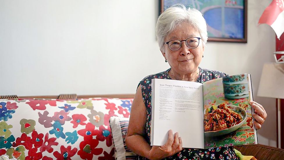 Lee Geok Boi holding her recipe book, In a Straits-Born Kitchen (Credit: Rachel Phua)