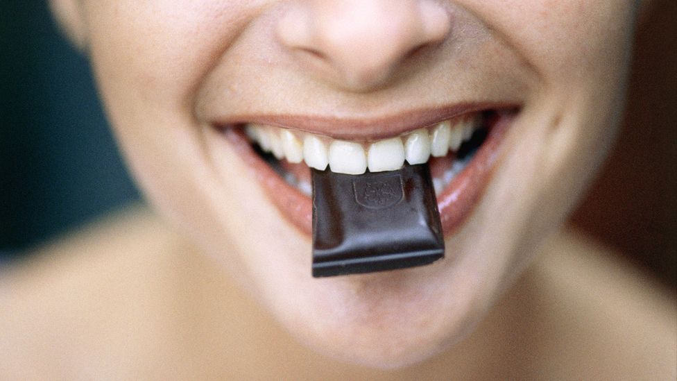 Smiling woman with chocolate square in mouth (Credit: Roy Morsch/Getty Images)