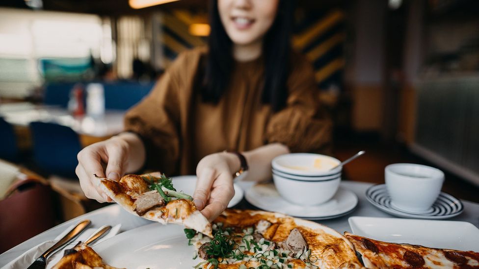 Young woman holding slice of pizza (Credit: Yiu Yu Hoi/Getty Images)