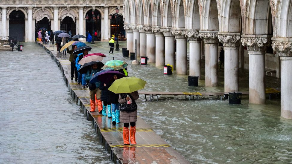 People walk on a footbridge across a flooded waterfront in Venice on November 24, 2019 during an "acqua alta" high tide (Credit: M.Medina/Getty Images)