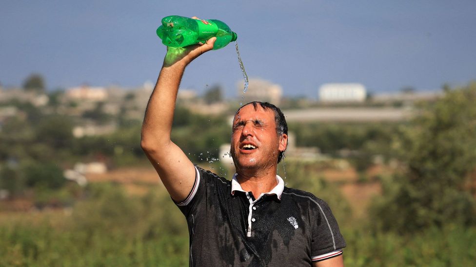 Outdoor worker pours water from a bottle onto his head to cool down during heat wave