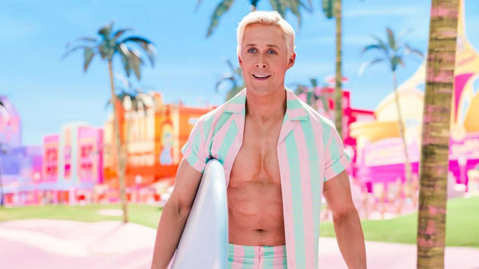 Ryan Gosling as Ken in the film Barbie, holding a surfboard