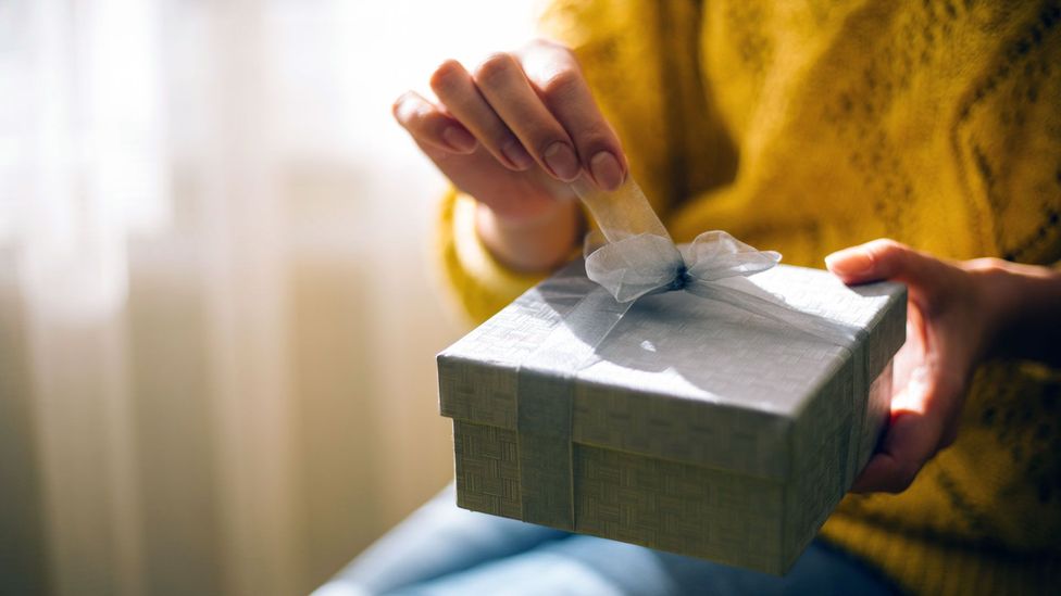 woman's hand in yellow sweater opening a box corporate gift reward program