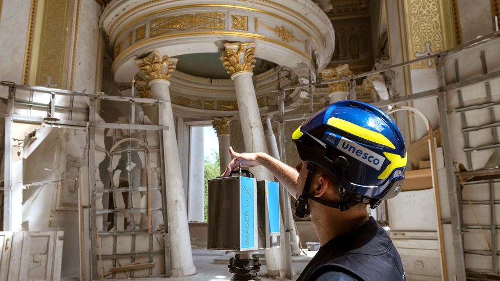 A Unesco consultant in a hard hat films a cathedral damaged by war