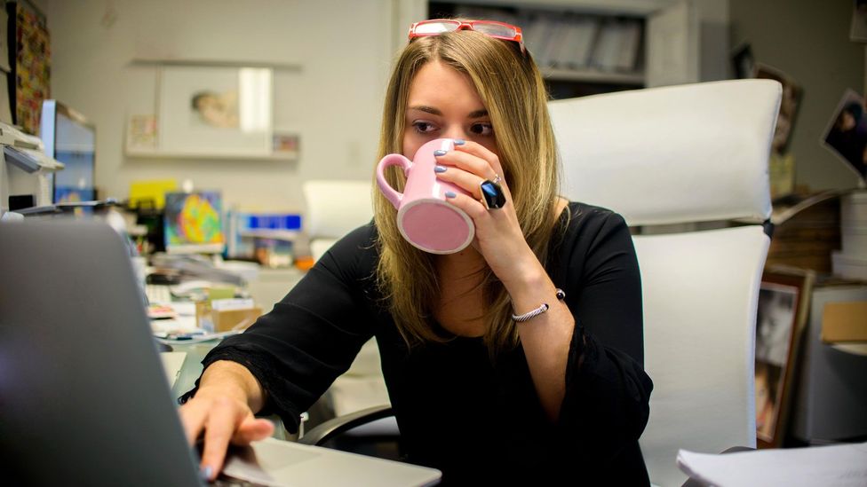 Woman drinking coffee from pink mug at desk