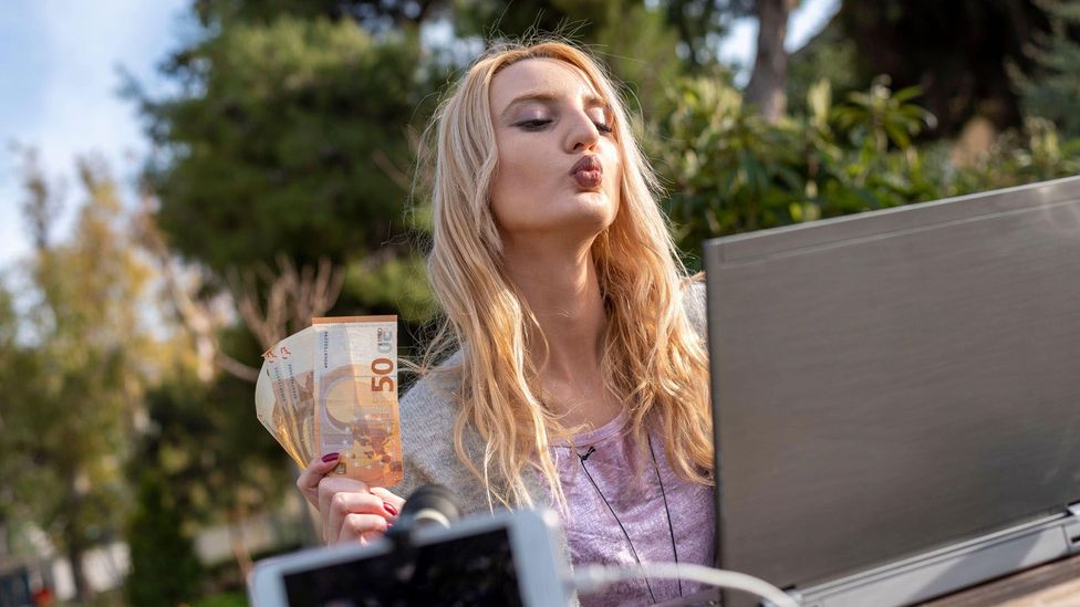 blonde woman influencer with money finance in front of laptop giving advice