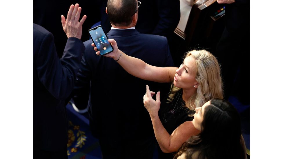 Η Marjorie Taylor Greene κρατά το τηλέφωνό της ενώ ο Ντόναλντ Τραμπ κρέμεται (Πηγή εικόνας: Getty Images)