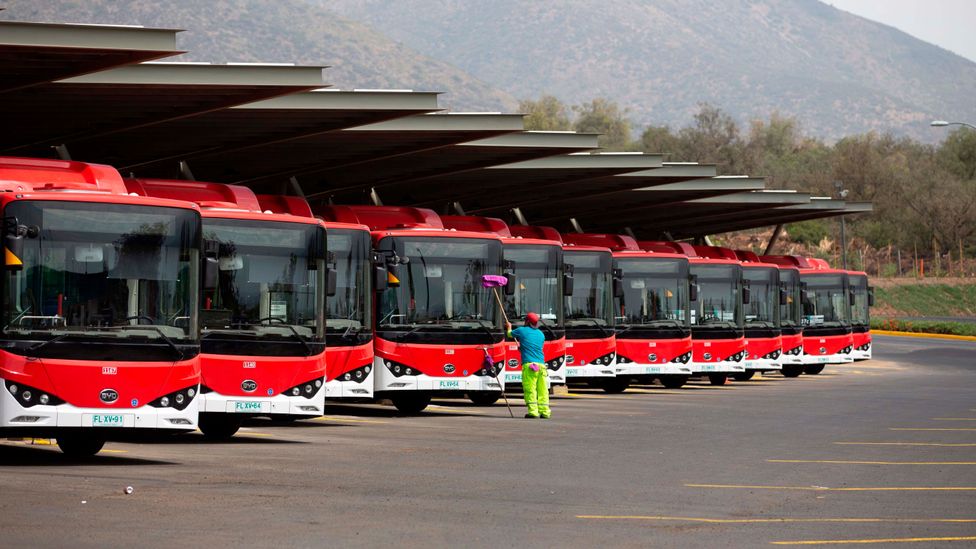 A row of red electric buses line up in a depot