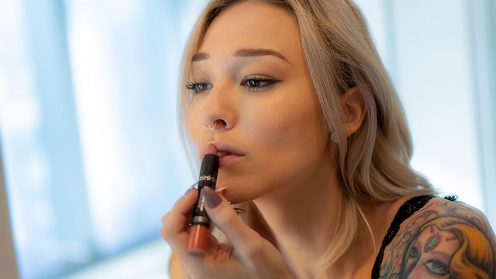 Woman putting on lipstick in mirror