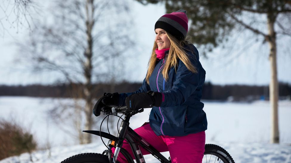 A woman in warm clothing on a mountain bike in the snow