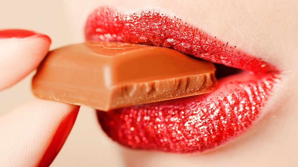 Close up of a woman's mouth as she bites into a square of chocolate (Credit: Getty Images)