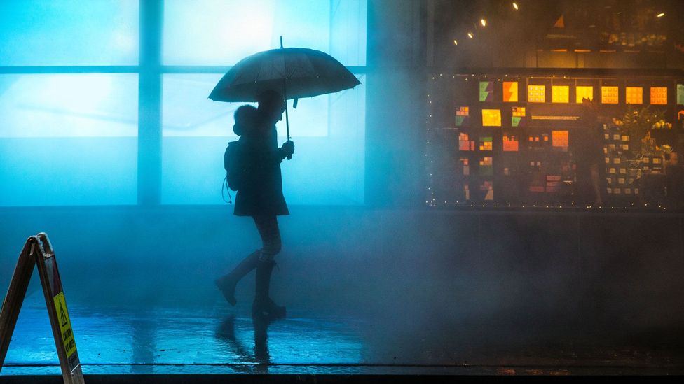 A woman holding an umbrella on a city street at night (Credit: Getty Images)