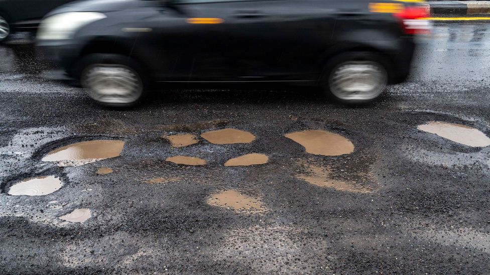 A car drives past some water filled potholes in a road (Credit: Getty Images)