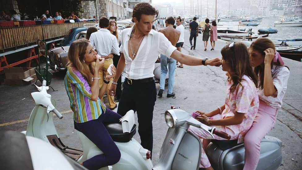 A young Italian man tweaks the nose of a young women on a scooter while talking to other young women (Credit: Getty Images)