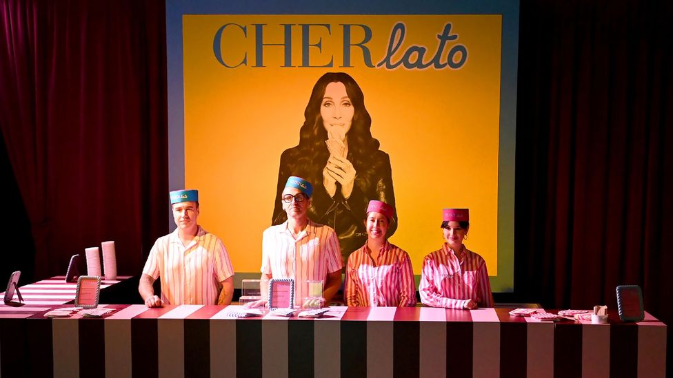 Four people stood in front of a sign for Cher's gelato business (Credit: Getty Images)
