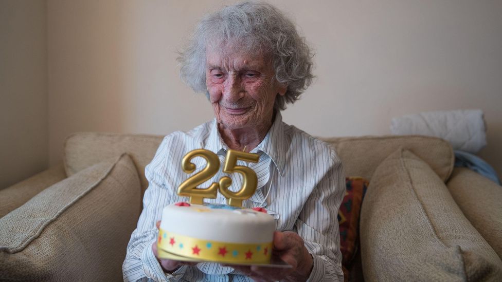 100 year old Doris Cleife holds a birthday cake with the number 25 (Credit: Alamy)