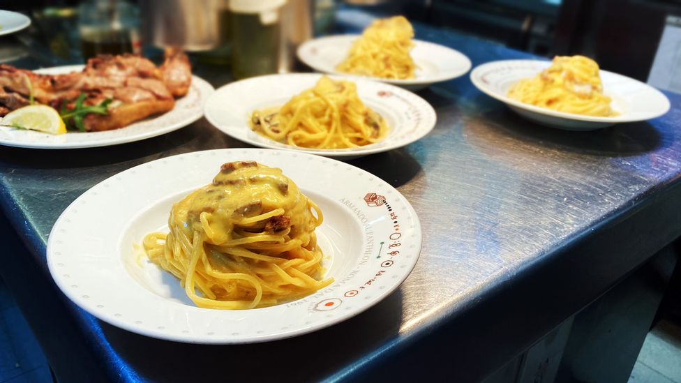 Four plates of carbonara in Armando al Pantheon's kitchen, waiting to be topped with a healthy shaving of cheese (Credit: Andrea Carlo Martinez)