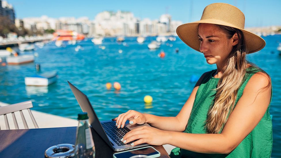 Woman in a hat working on her laptop by the ocean (Credit: Getty Images)