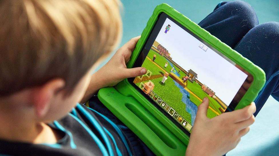 A young boy sits on the floor while playing Minecraft on a tablet (Credit: Alamy)