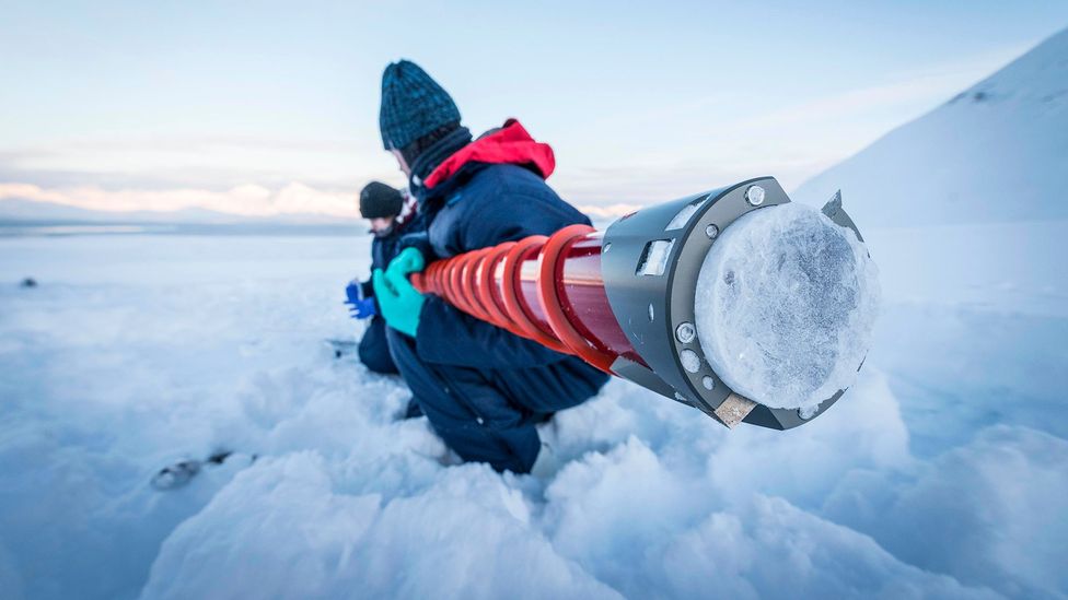 Dr Liam Kelleher and Alice Philips from University of Birmingham stood in the snow, holding a research instrument, in Ny-Ålesund in Norway (Credit: Iain Rudkin)